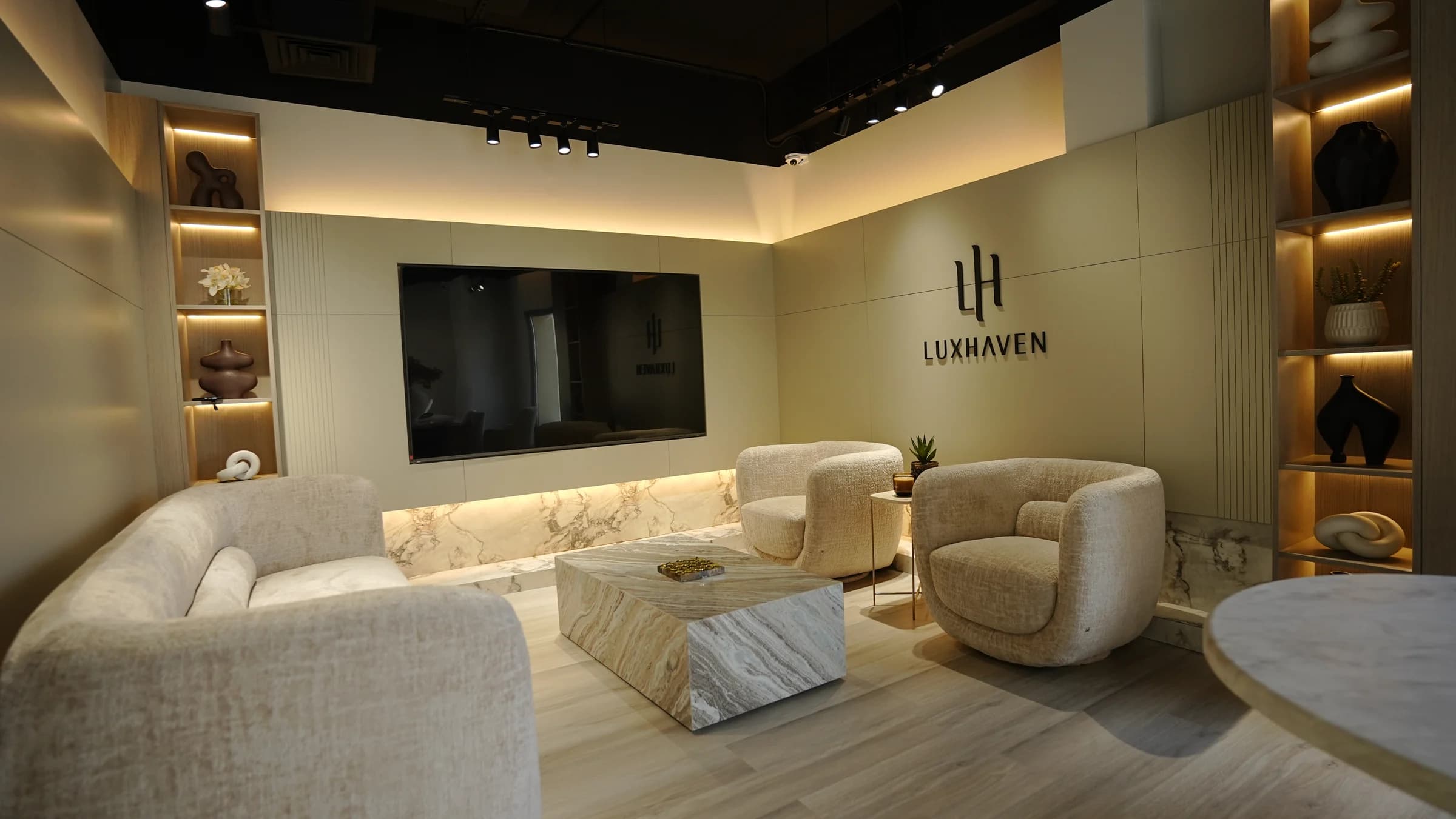 The seating area inside Luxhaven, with lounge chairs, a marble table and the Luxhaven wall logo