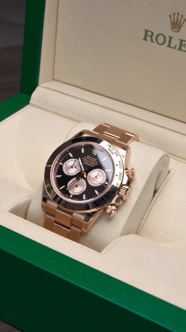 A rose-gold-tone Rolex Daytona with a black dial displayed inside an open green watch box.