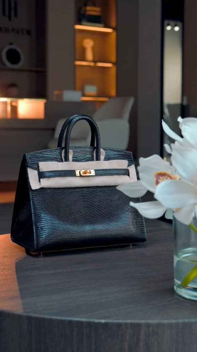 A black textured handbag with gold-tone hardware beside white flowers in the Luxhaven showroom.
