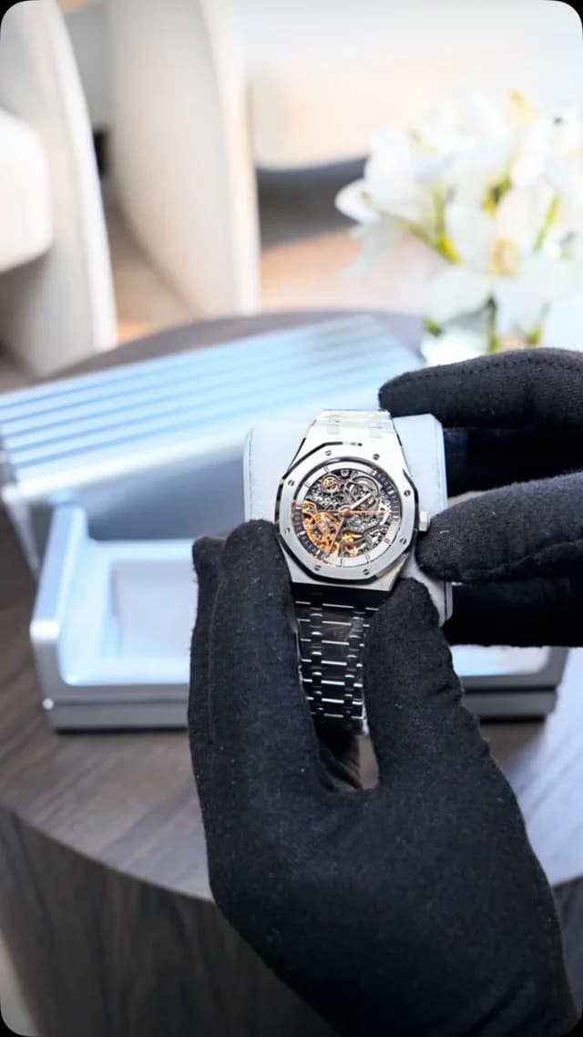 Gloved hands presenting a skeleton-dial watch on a cushion at Luxhaven.